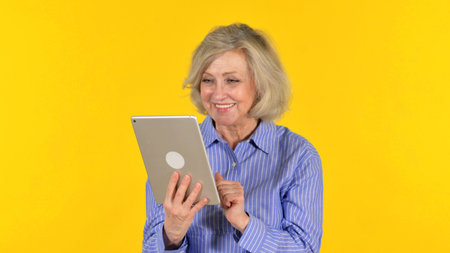 Old Woman Doing Video Chat on Tablet on Yellow Background