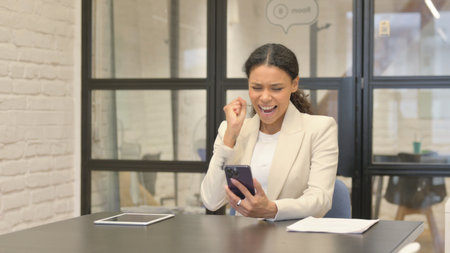 African Business Woman Celebrating Success on Phone in Officeの写真素材