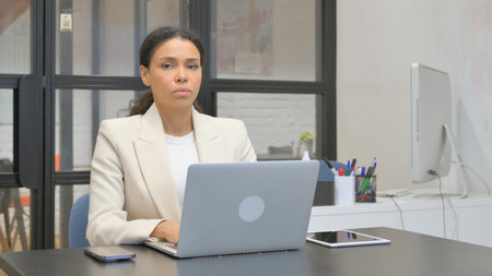 African Business Woman Looking at Camera while Working on Laptop in Officeの写真素材