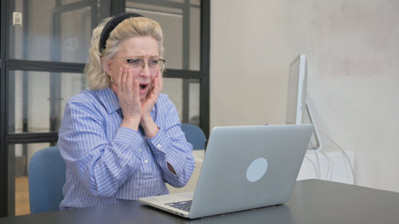 Casual Old Woman Reacting to Online Loss at Workの写真素材