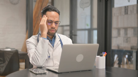 Working African Male Doctor having Headache in Clinicの写真素材