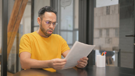 Creative Mixed Race Man Feeling Upset while Reading Contractの写真素材
