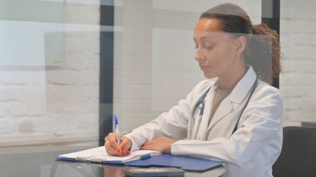 Multiracial Female Doctor Writing Medical Report in Hospitalの写真素材