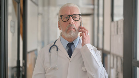 Portrait of Senior Male Doctor Talking on Phone in Hospitalの写真素材