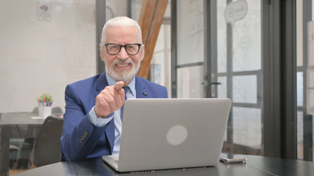Senior Old Businessman Pointing at Camera at Workplace