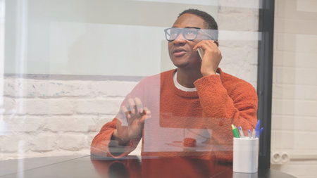 Young african american man in glasses talking on mobile phone at home