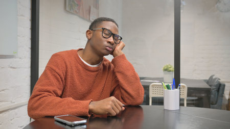 Young african american man with eyeglasses sitting at table and thinkingの写真素材