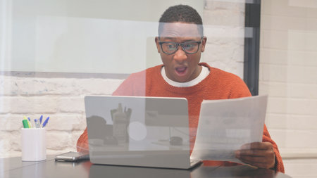 Shocked African Man Working on Documents and Laptop