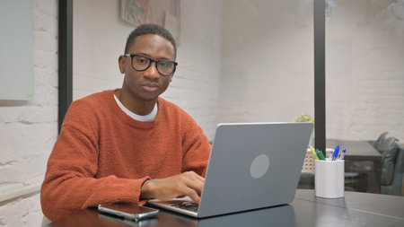 Young african american man working on laptop at home office.