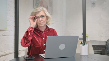Senior Adult Woman Looking Seriously at Camera while Working on Laptop