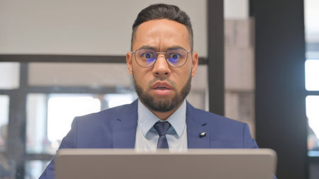 Close up of Hispanic Businessman Shocked at Camera while Using Laptopの写真素材
