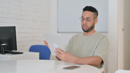 Hispanic Man Doing Video Chat on Tablet at Workspaceの写真素材