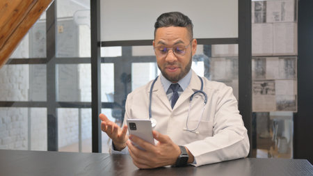 Online Video Chat by Hispanic Doctor on Phone in Clinicの写真素材