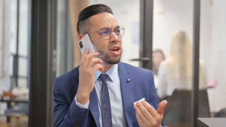 Portrait of Angry Hispanic Businessman Talking on Phone