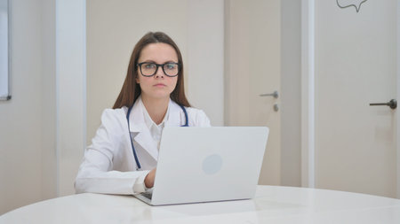 Young Doctor Looking at Camera while Using Laptopの写真素材