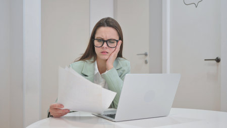 Upset Young Woman Cursing while Working on Laptop and Documents