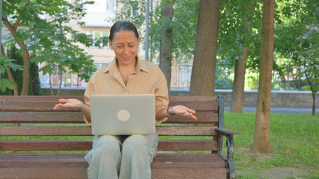 Perplexed Multi Ethnic Woman Using Laptop on Park Benchの写真素材