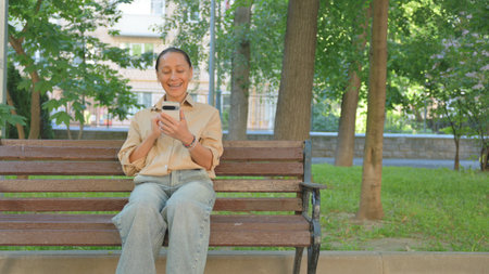 Multi Ethnic Woman Video Calling or Conferencing on a Phone on a Park Benchの写真素材