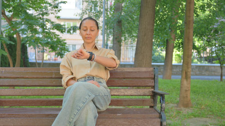 Waiting Multi Ethnic Woman Checking Wrist Watch on Park Benchの写真素材