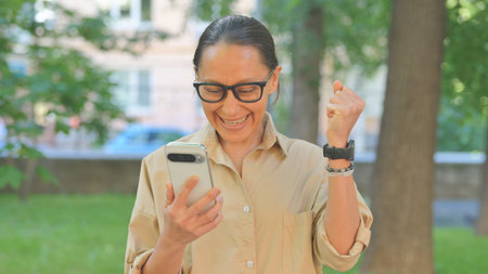 Multi Ethnic Woman Celebrating with Phone Outdoorsの写真素材