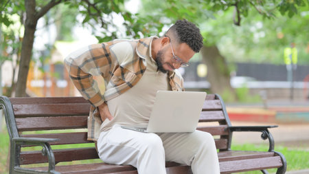 Hispanic Man with Back Pain While Using Laptop in Park