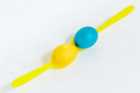 Easter eggs lie on plastic yellow spoons, isolated on a white background.