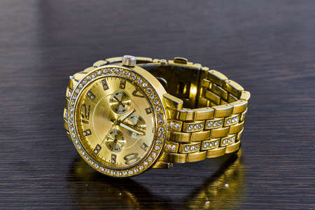 Gilded wristwatch for women with studio lighting, lying on a dark background.