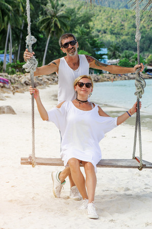 mature couple rest on a swing at tropical beachの写真素材