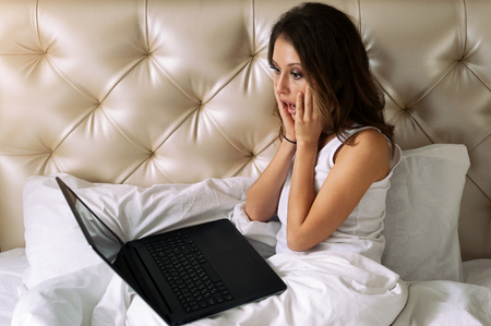Young woman shoked looking in laptop sitting in the bedの写真素材
