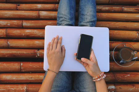 woman with a laptop holding a phone in her hand on bamboo floorの写真素材