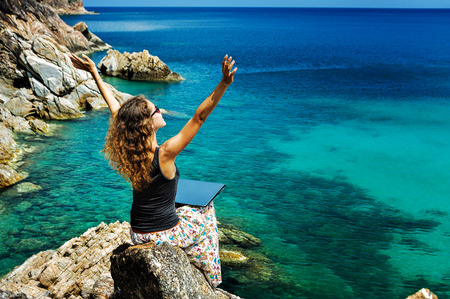 Happy lady freelancer sitting with laptop on a high and raising her arms upの写真素材