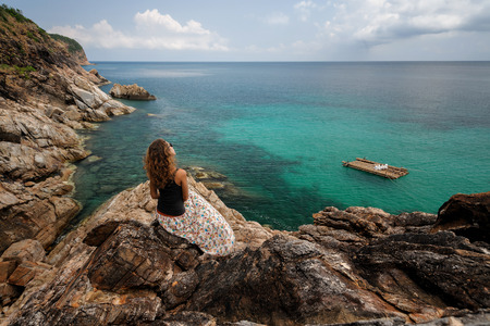 Happy woman freelancer with laptop is sitting on the stone on high in front of amazing seaview with blue lagoon surrounded with rocksの写真素材