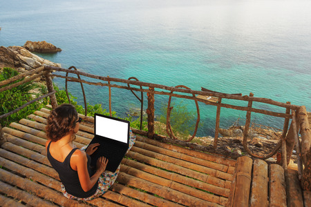 Woman freelancer sitting with laptop in bamboo alcove on a high. Amazing sea-view with blue lagoon.の写真素材