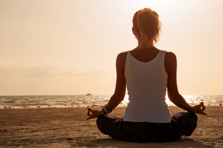 Silhouette young woman practicing yoga on the beach at sunset.の写真素材