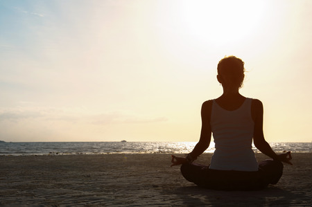 Silhouette young woman practicing yoga on the beach at sunset.の写真素材
