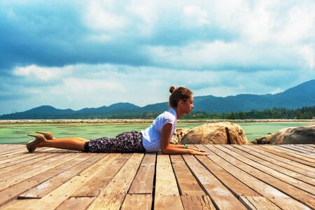 Woman in office suit doing yoga on the wooden floor with laptop. Young Lady has practice on the beach in front of sea view.の写真素材