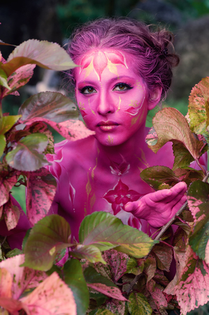 Woman in pink paint. Attractive and sexy girl. Face art. Bright make up and body art. Flowers ornament. jungle background.の写真素材