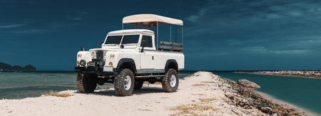 Panoramic photo of safari car on offroad , adventure trail. ocean, sky and clouds on background, With empty space for logo or textの写真素材