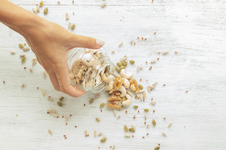 female hand is scattering Seeds and nuts from the jarの写真素材