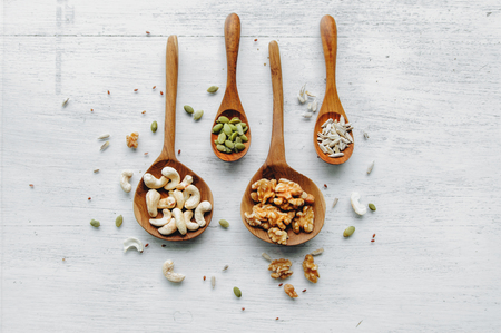Four wooden spoons with seeds and nuts on the white tableの写真素材
