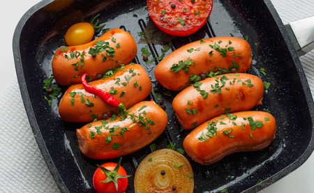 Fried sausages with herbs and vegetables in grill pan at white background. Top view copy space.の写真素材