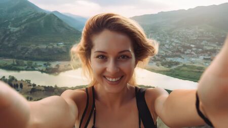 Beautiful young woman doing selfie in the mountains with river on background in Georgiaの写真素材