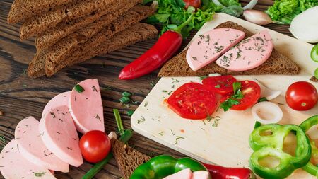 sandwich of rye bread with boiled sausage and vegetables on a rustic wooden backgroundの写真素材