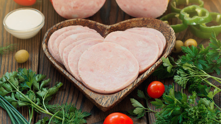 Vegetables and Cutted Ham Sausage in heart plate on wooden background, selective focusの写真素材
