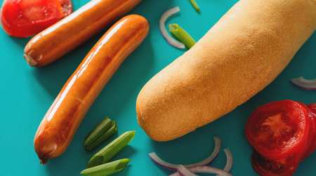 two grilled sausages with vegetables and bread for hot dog on blue backgroundの写真素材