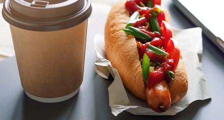 hotdog and cup of coffee near laptopの写真素材