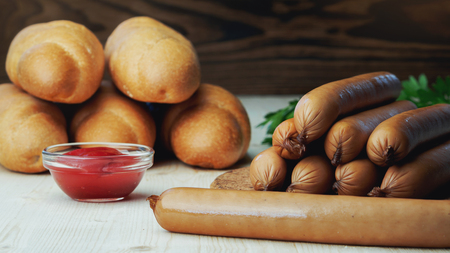 Ingredients for making homemade hot dogs. Sausages, fresh baked buns and ketchup sauce, served on wood chopping board over wooden background. Rustic styleの写真素材