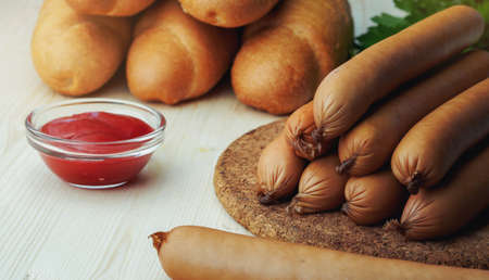 Ingredients for making homemade hot dogs. Sausages, fresh baked buns and ketchup sauce, served on wood chopping board over wooden background. Rustic styleの写真素材