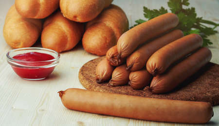 Ingredients for making homemade hot dogs. Sausages, fresh baked buns and ketchup sauce, served on wood chopping board over wooden background. Rustic styleの写真素材