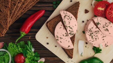 sandwich of rye bread with boiled sausage and vegetables on a rustic wooden backgroundの写真素材